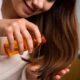 A woman applies argan oil to her damp hair in front of a mirror during dry winter weather