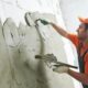 A worker smooths lime plaster on a lath wall with a flat trowel