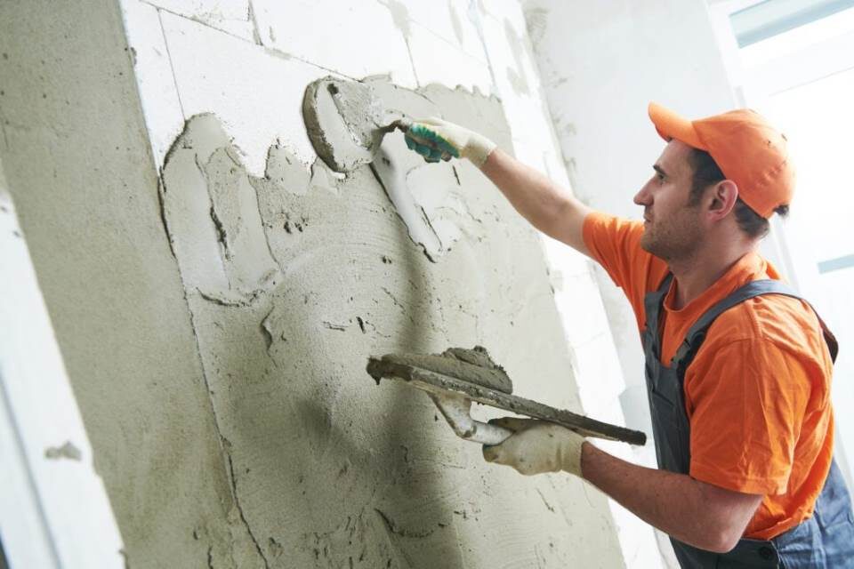 A worker smooths lime plaster on a lath wall with a flat trowel