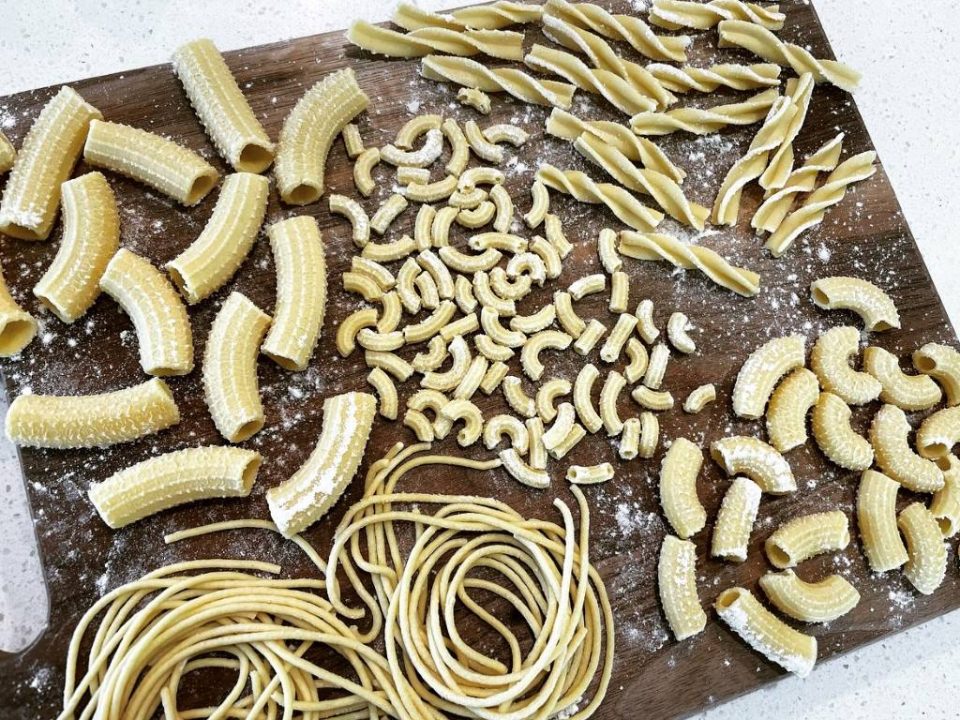 Italy pasta extruder creating perfect rigatoni strands dusted with semolina