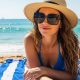 A woman wearing large UV-protective polarized sunglasses while relaxing on a sunny beach with the ocean in the background
