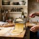 Compact manual pasta maker clamped to a small apartment kitchen counter with freshly rolled pasta dough sheets