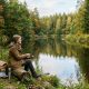 A person sitting peacefully on a riverbank holding a fishing rod surrounded by trees and calm water