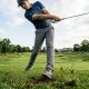 Golfer mid-swing wearing performance shoes firmly planted on green grass.