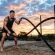 Athlete training arms intensely with heavy fitness ropes outdoors.