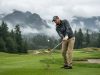 A male golfer swinging an iron club on a scenic Washington golf course.